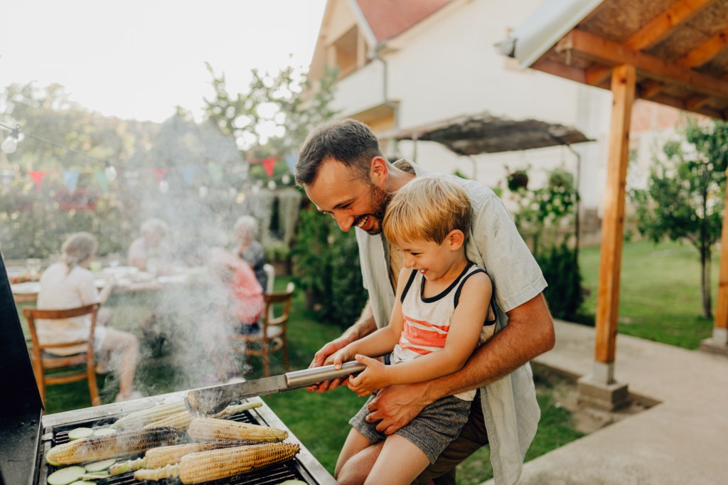 Dad showing his son how to grill during an outdoor party.
