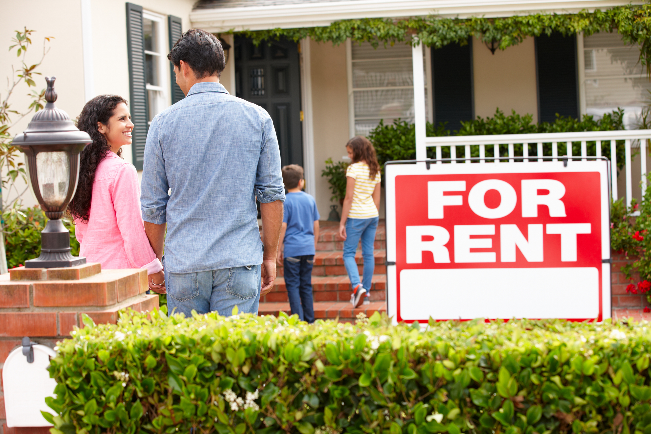 Hispanic family outside home for rent holding hands looking at each other happy.