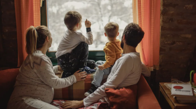 Family looking at snow falling outside.