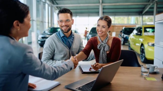 Couple shaking hands with saleswoman after buying a new car.