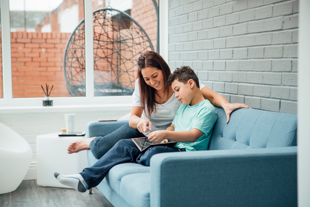 A little boy and his mom reading a book together in the living room.