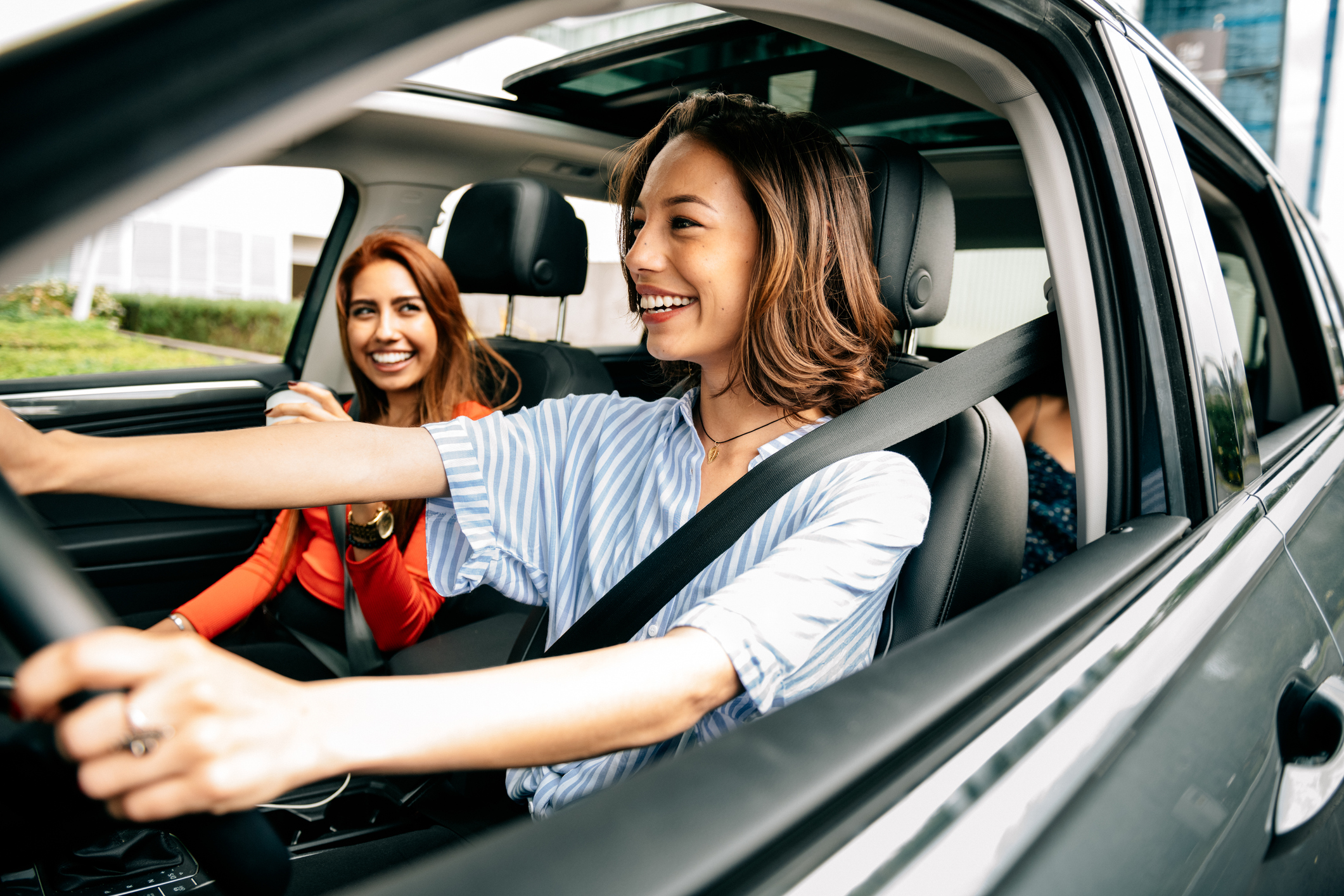 Two happy women driving in a car with their window down.